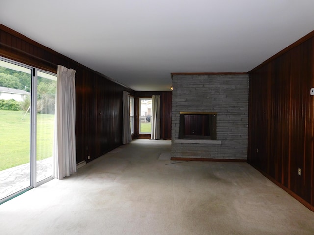 unfurnished living room featuring a large fireplace, light carpet, wood walls, and a healthy amount of sunlight