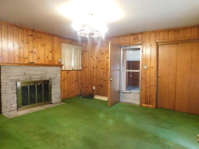 unfurnished living room featuring a baseboard heating unit, carpet floors, a stone fireplace, and wood walls