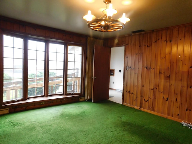 carpeted empty room with a baseboard heating unit, a notable chandelier, wood walls, and visible vents