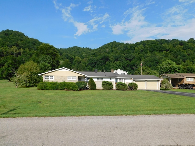 ranch-style home with a garage, a front lawn, driveway, and a wooded view