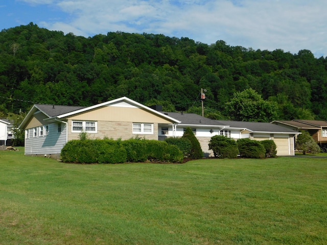 ranch-style home with an attached garage, a wooded view, and a front yard