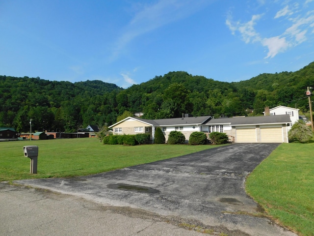 view of front of property featuring an attached garage, aphalt driveway, a wooded view, and a front yard