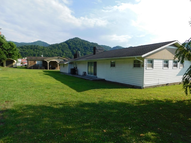 rear view of property with a chimney, a mountain view, and a lawn