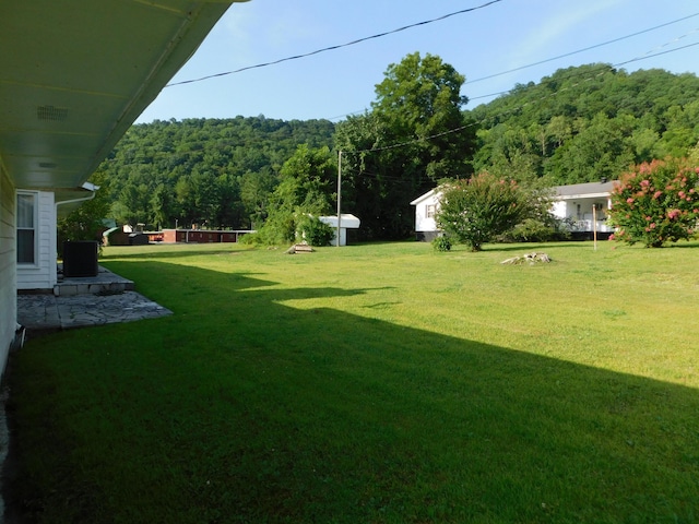 view of yard with a wooded view and central air condition unit