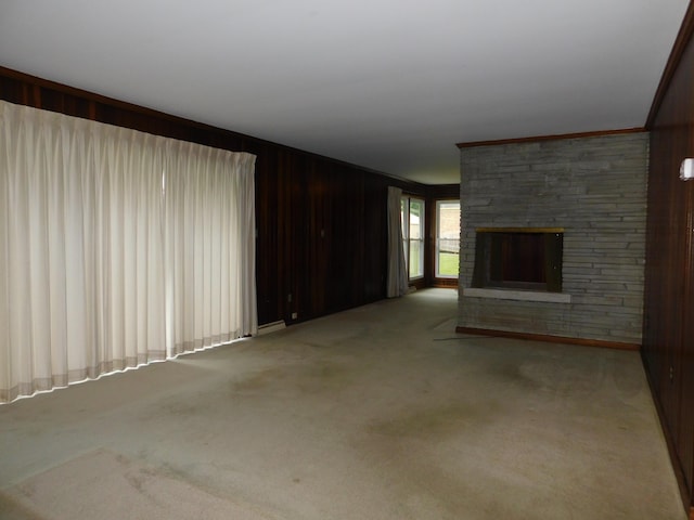 unfurnished living room featuring ornamental molding, carpet flooring, a fireplace, and wood walls