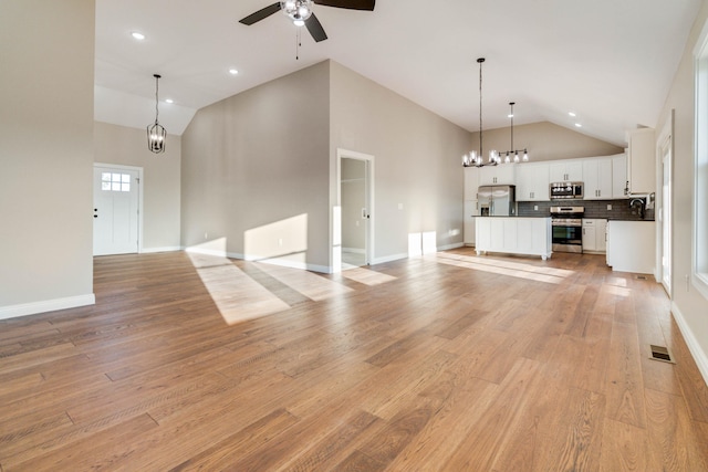 unfurnished living room with light hardwood / wood-style flooring, ceiling fan with notable chandelier, and high vaulted ceiling