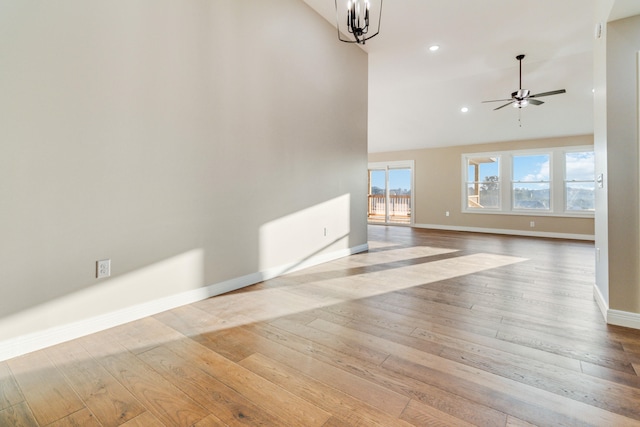 unfurnished living room with high vaulted ceiling, ceiling fan with notable chandelier, and light wood-type flooring