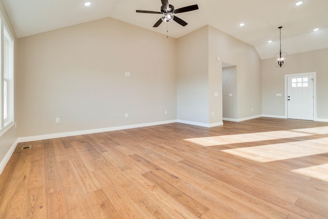 unfurnished living room with high vaulted ceiling, ceiling fan with notable chandelier, and light hardwood / wood-style floors