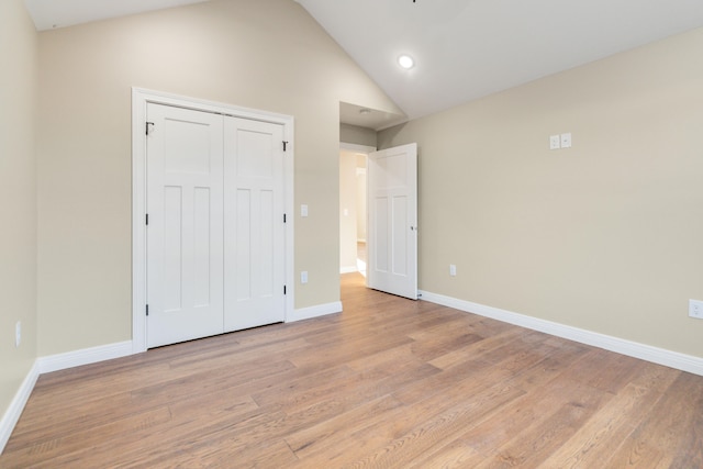 unfurnished bedroom featuring light hardwood / wood-style floors, lofted ceiling, and a closet