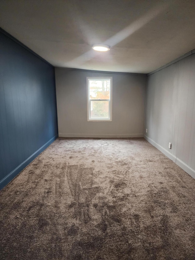 carpeted empty room featuring wood walls