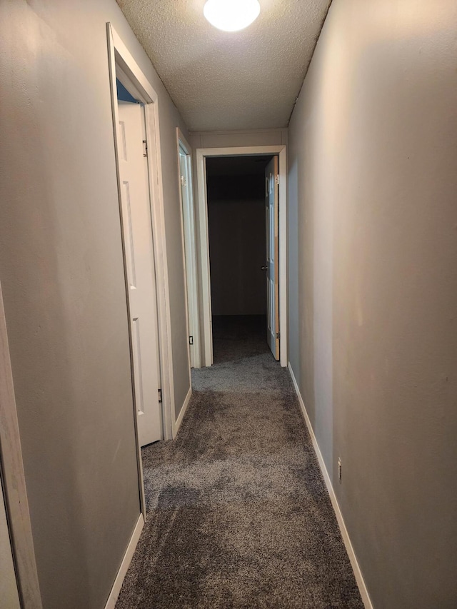 corridor with a textured ceiling and dark carpet