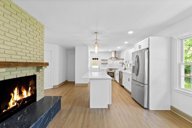 kitchen with appliances with stainless steel finishes, wall chimney exhaust hood, pendant lighting, a fireplace, and white cabinetry