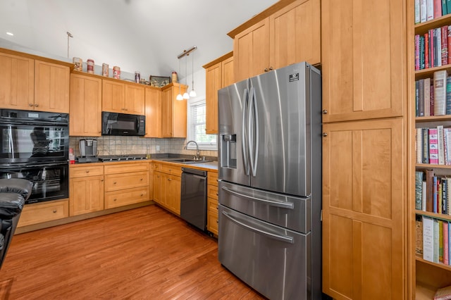 kitchen featuring decorative backsplash, light wood-type flooring, sink, black appliances, and decorative light fixtures