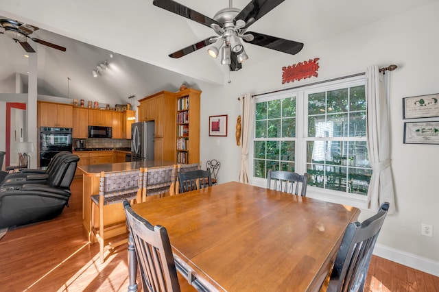 dining space with ceiling fan, light hardwood / wood-style flooring, a wealth of natural light, and vaulted ceiling