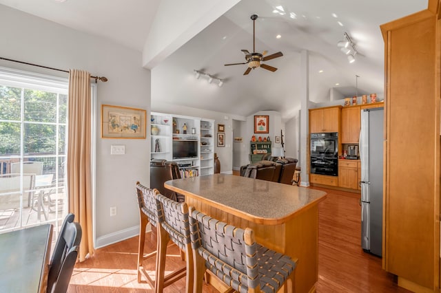 kitchen with stainless steel fridge, light wood-type flooring, a kitchen breakfast bar, vaulted ceiling, and ceiling fan