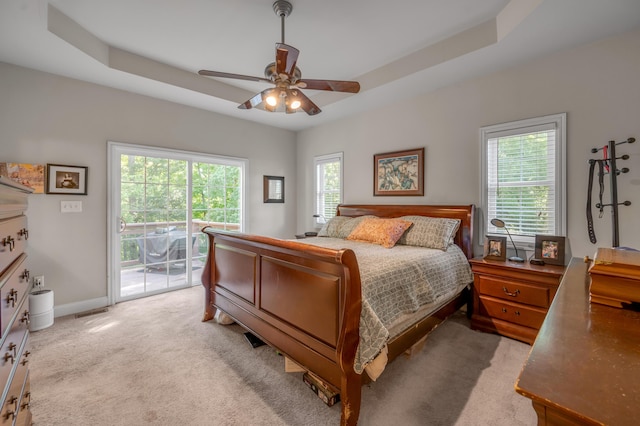 carpeted bedroom featuring ceiling fan, a raised ceiling, access to outside, and multiple windows