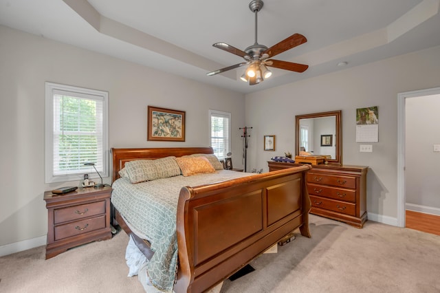 bedroom featuring a raised ceiling, ceiling fan, and light carpet