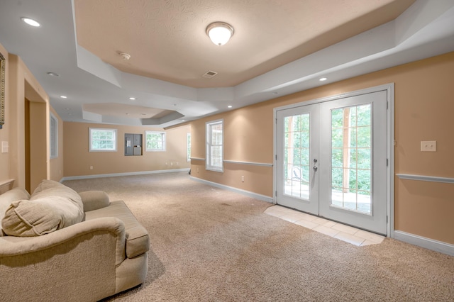 living room with a tray ceiling, french doors, and light colored carpet