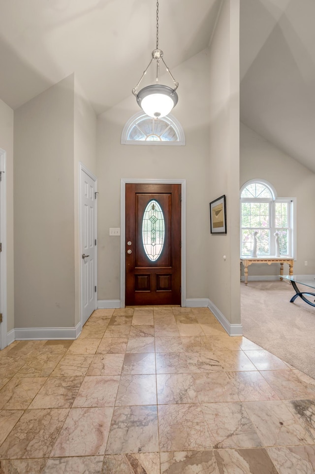 carpeted foyer entrance featuring high vaulted ceiling