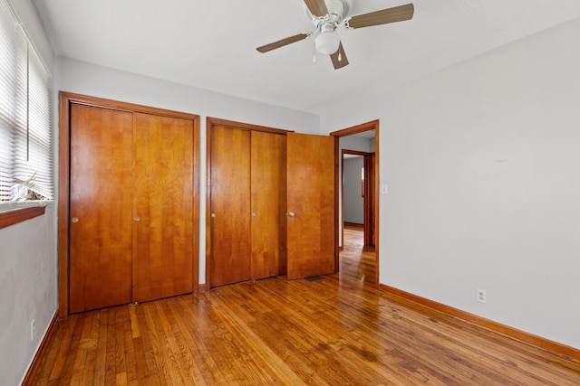 unfurnished bedroom featuring multiple closets, multiple windows, ceiling fan, and hardwood / wood-style floors