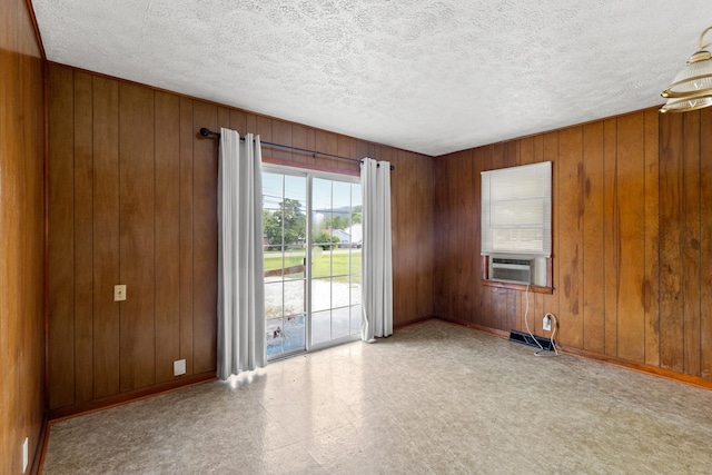 spare room with a textured ceiling, wooden walls, and cooling unit