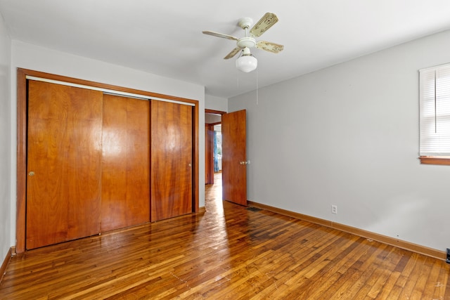 unfurnished bedroom with a closet, multiple windows, ceiling fan, and hardwood / wood-style floors