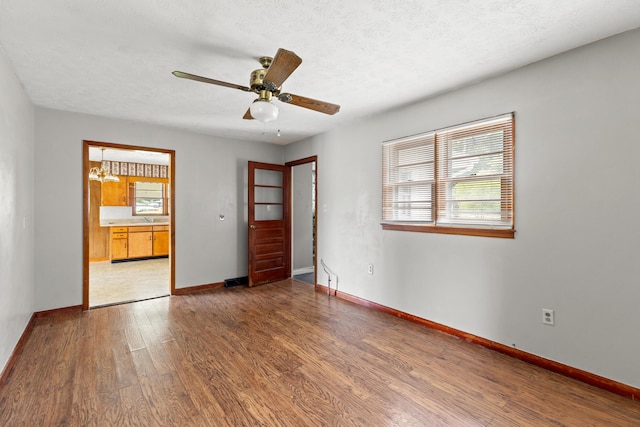 unfurnished room featuring ceiling fan with notable chandelier, a textured ceiling, hardwood / wood-style flooring, and a healthy amount of sunlight