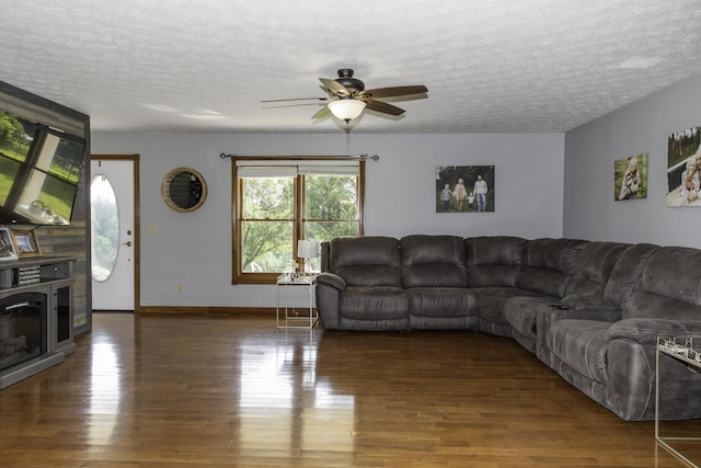 living room with a textured ceiling, ceiling fan, and dark wood-type flooring