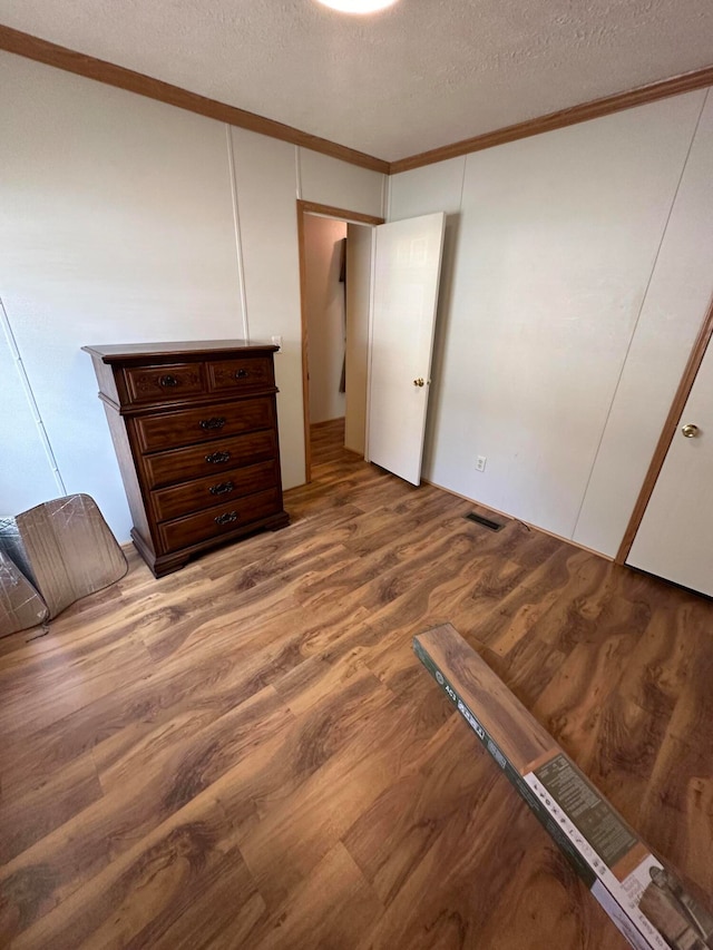 unfurnished bedroom with hardwood / wood-style flooring, crown molding, and a textured ceiling