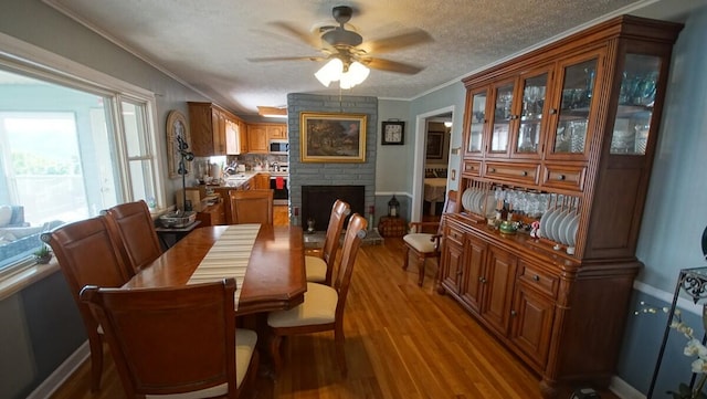 dining space featuring a textured ceiling, a large fireplace, ceiling fan, wood-type flooring, and ornamental molding