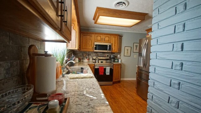 kitchen with hardwood / wood-style flooring, ornamental molding, sink, light stone countertops, and appliances with stainless steel finishes