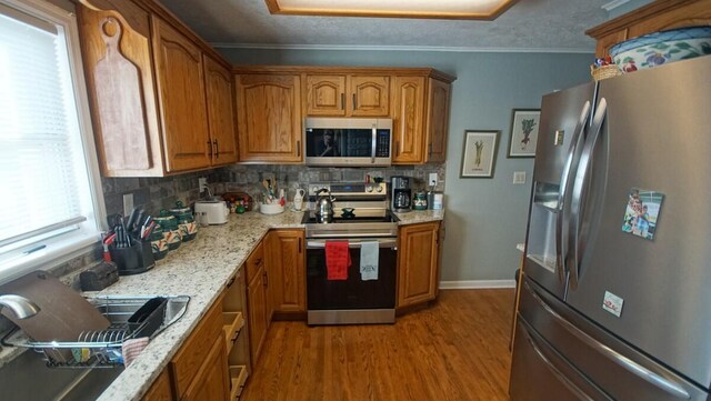 kitchen with decorative backsplash, appliances with stainless steel finishes, light stone countertops, and hardwood / wood-style flooring