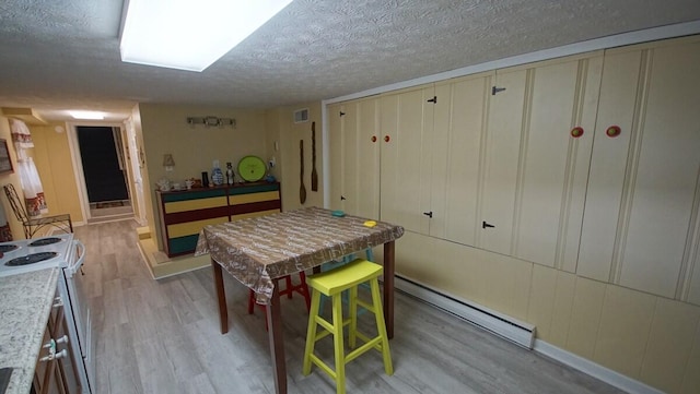 dining space featuring light hardwood / wood-style flooring, a textured ceiling, and a baseboard heating unit