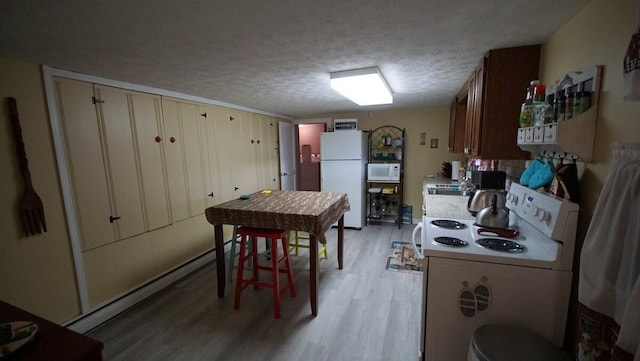 kitchen featuring white appliances, a textured ceiling, cream cabinetry, a baseboard radiator, and wood-type flooring