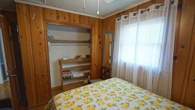 bedroom with wooden walls, multiple windows, a closet, and ornamental molding