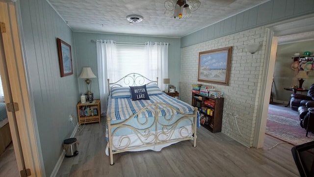 bedroom with brick wall, a textured ceiling, and wood-type flooring