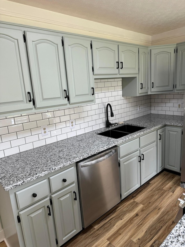 kitchen featuring dishwasher, sink, hardwood / wood-style flooring, light stone countertops, and a textured ceiling