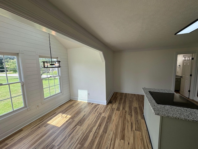 unfurnished dining area featuring lofted ceiling, wooden walls, light hardwood / wood-style floors, a textured ceiling, and a chandelier