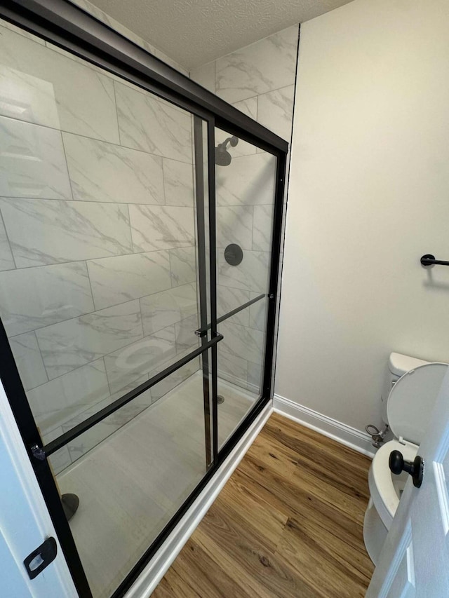 bathroom featuring walk in shower, wood-type flooring, toilet, and a textured ceiling