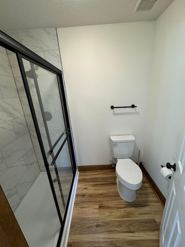 bathroom featuring an enclosed shower, hardwood / wood-style floors, a textured ceiling, and toilet