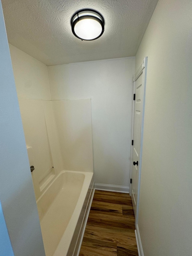 bathroom with hardwood / wood-style flooring, a textured ceiling, and a bathtub