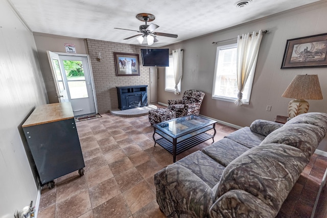 tiled living room featuring brick wall, a wood stove, a healthy amount of sunlight, and ceiling fan