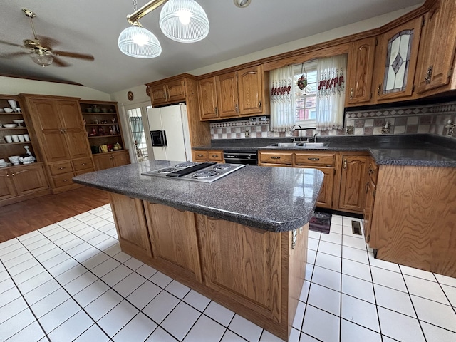 kitchen featuring white refrigerator with ice dispenser, a kitchen island, stainless steel gas cooktop, backsplash, and sink