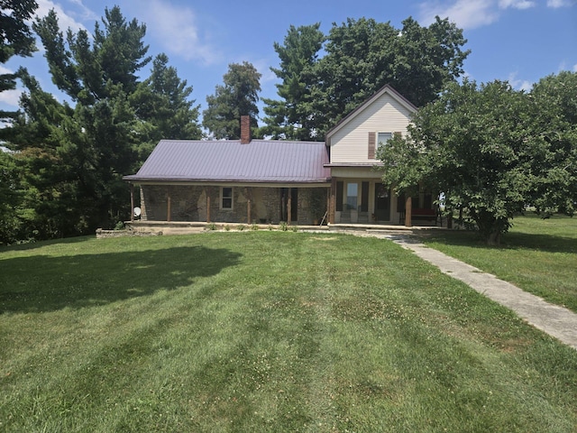 view of front of property featuring a front yard, covered porch, metal roof, and a chimney