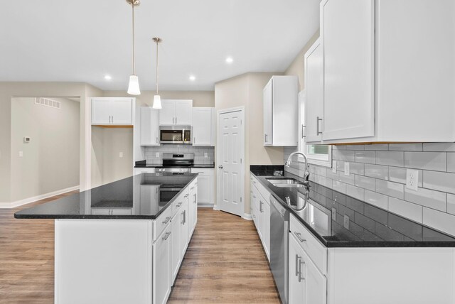 kitchen with appliances with stainless steel finishes, white cabinets, sink, and a kitchen island