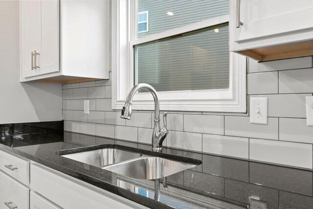 kitchen featuring sink, white cabinetry, dark stone counters, and decorative backsplash