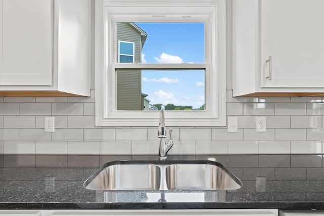 kitchen featuring white cabinets, dark stone countertops, backsplash, and sink