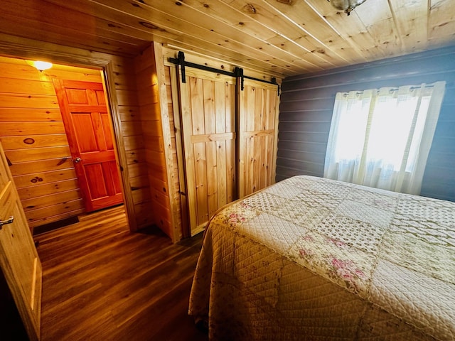 bedroom with dark wood-type flooring, wood ceiling, a barn door, and wooden walls