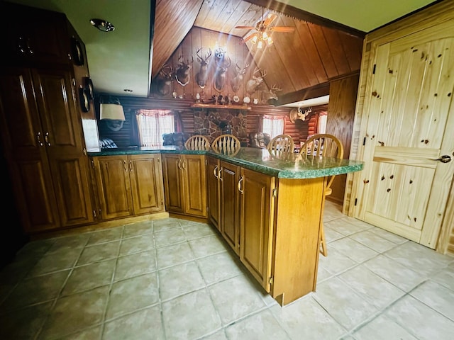 kitchen with wood walls, kitchen peninsula, ceiling fan, light tile patterned flooring, and lofted ceiling