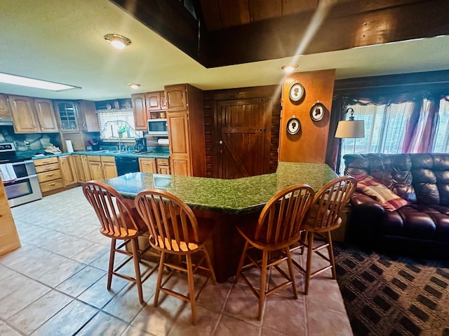 kitchen with exhaust hood, light tile patterned floors, a kitchen bar, appliances with stainless steel finishes, and sink